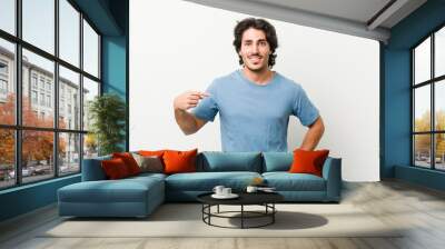 Young handsome man against a white background person pointing by hand to a shirt copy space, proud and confident Wall mural