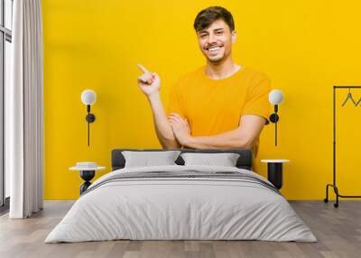 Young hispanic casual man smiling cheerfully pointing with forefinger away. Wall mural