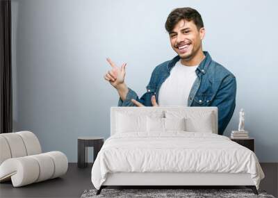 Young hispanic cool man pointing with forefingers to a copy space, expressing excitement and desire. Wall mural