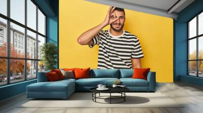 Young Hispanic man on yellow background excited keeping ok gesture on eye. Wall mural