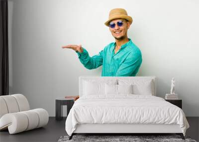 Young hispanic man wearing a summer clothes shocked and amazed holding a copy space between hands. Wall mural