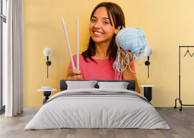 Young hispanic woman holding a ball of wool isolated on yellow background Wall mural