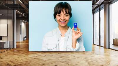 Young hispanic woman holding a batterie isolated on blue background happy, smiling and cheerful. Wall mural