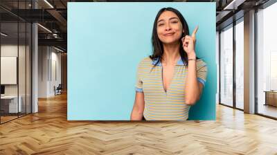 Young hispanic woman isolated on blue background showing number one with finger. Wall mural