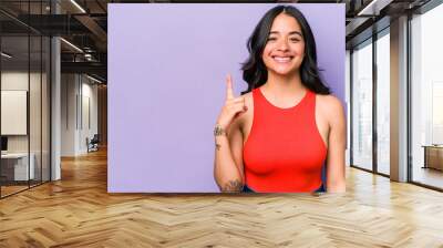 Young hispanic woman isolated on purple background showing number one with finger. Wall mural