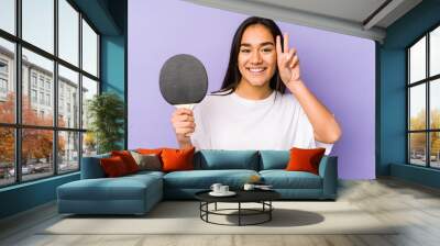 Young indian woman playing ping pong isolated showing victory sign and smiling broadly. Wall mural