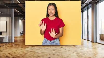 Young Indonesian woman on yellow studio backdrop rejecting someone showing a gesture of disgust. Wall mural