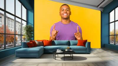 Young latin man isolated on yellow background indicates with both fore fingers up showing a blank space. Wall mural