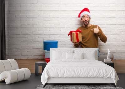 Young man sitting with gifts celebrating christmas surprised, feels successful and prosperous Wall mural