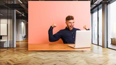 Young man working with his laptop raising fist after a victory, winner concept. Wall mural