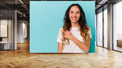 Young mexican woman isolated on blue background smiling and pointing aside, showing something at blank space. Wall mural