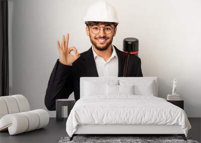 Young mixed race architect man wearing a helmet isolated on grey background cheerful and confident showing ok gesture. Wall mural