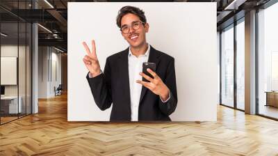 Young mixed race business man holding mobile phone isolated on white background joyful and carefree showing a peace symbol with fingers. Wall mural