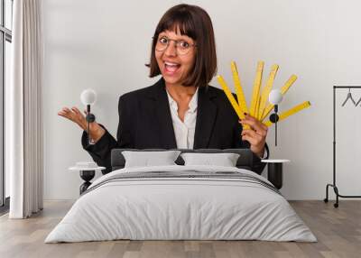 Young mixed race business woman holding a measure tape isolated on white background receiving a pleasant surprise, excited and raising hands. Wall mural