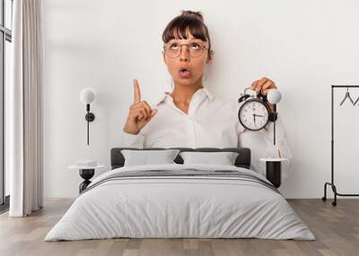 Young mixed race business woman holding an alarm clock isolated on white background  pointing upside with opened mouth. Wall mural