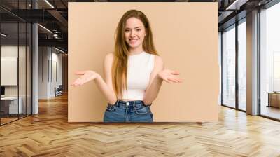 Young redhead woman cut out isolated makes scale with arms, feels happy and confident. Wall mural