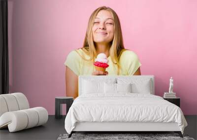 Young russian woman eating an ice cream isolated laughs and closes eyes, feels relaxed and happy. Wall mural