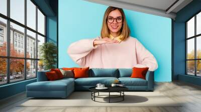 Young student caucasian woman isolated on blue background holding something with both hands, product presentation. Wall mural