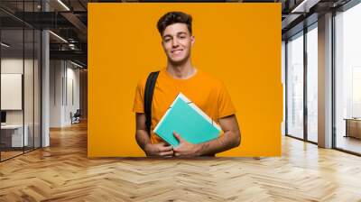 Young student man holding books smiling and raising thumb up Wall mural