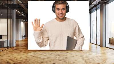 Young student man with a laptop smiling cheerful showing number five with fingers. Wall mural