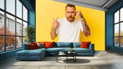 Young tattooed caucasian man isolated on yellow background showing a disappointment gesture with forefinger. Wall mural