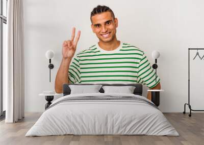 Young venezuelan man isolated on white background showing victory sign and smiling broadly. Wall mural