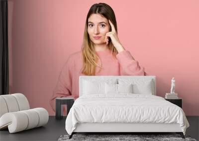 Young woman holding a container of coffee beans, symbolizing the energy and invigoration of this beloved beverage pointing temple with finger, thinking, focused on a task. Wall mural