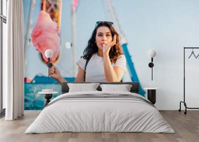 Funny young woman eating cotton candy at fairground Wall mural