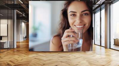 Healthy beautiful young woman holds a glass of water in kitchen, smiling young girl drinking fresh water from glass Wall mural