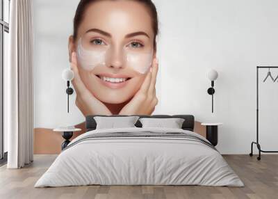 Portrait of beautiful woman smiling and applying face cream isolated over white background Wall mural