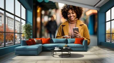 Portrait of beautiful young woman walking in the city holding phone, happy Young woman using smartphone walking through city street Wall mural