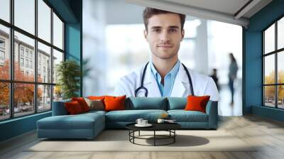 Portrait of young man doctor with stethoscope at bright white hospital room. medical male doctor standing in front of blurred hospital background Wall mural