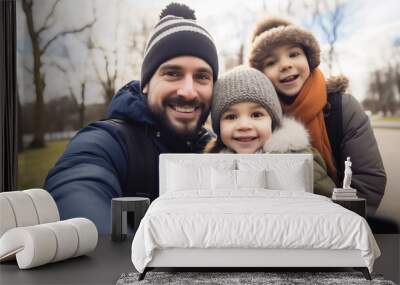 Smiling family taking a selfie outdoors in winter attire, capturing a joyful moment together in a park with bare trees in the background Wall mural