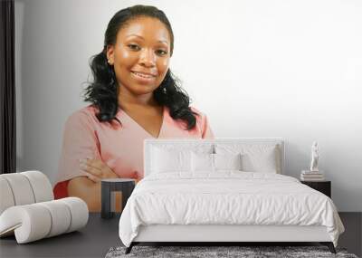 Attractive young African American female healthcare worker poses in pink scrubs against plain background - smiling with arms crossed Wall mural