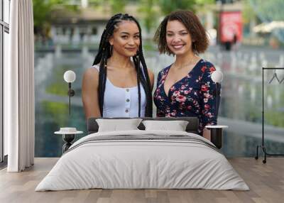 Two beautiful young multi-ethnic women pose for photos together in city on summer day Wall mural