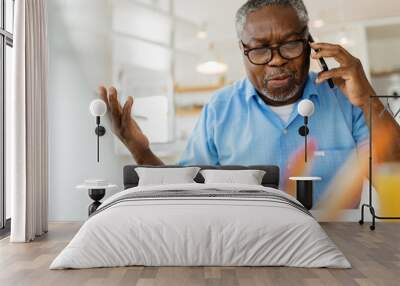 An old black man is sitting at his home office and having a phone conversation with customer support. Wall mural