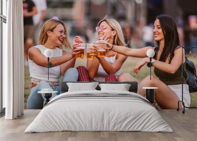 Girls sitting on the ground and cheering with beer at music festival Wall mural