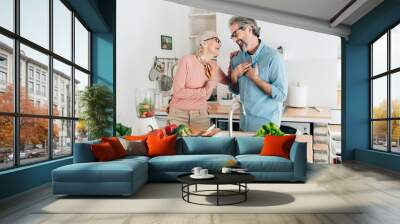 Senior couple preparing healthy smoothie in kitchen and using tablet to read recipe Wall mural