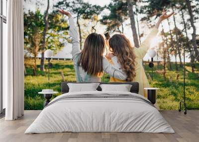 Two young women sitting on grass hugging rear view Wall mural