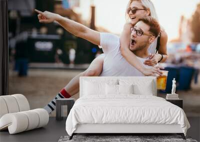 Young couple piggy backing at music festival  Wall mural