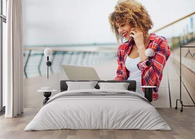 Young woman sitting at the stairs, working on laptop and talking on mobile phone Wall mural