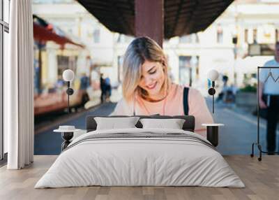 Young woman sitting at the train station and using mobile phone   Wall mural