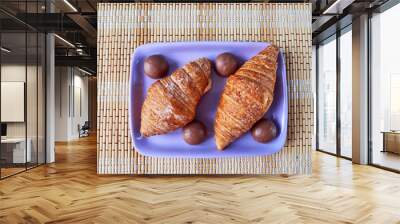 Two croissants and chocolate round candies lie on a lilac plate. Top view Wall mural