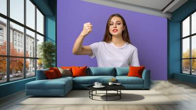 Angry brunette girl raising fist, sulking angry and tensed, frowning stare someone said rude words, standing in blank white t shirt over purple background. Young emotional woman Wall mural