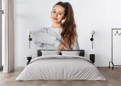 Happy young woman in white sweatshirt, pointing finger down, showing amazing news, promo banner, offer. Smiling brunette female stands against white studio background Wall mural