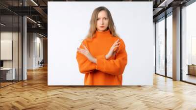 Portrait of woman showing stop gesture with crossed hands, disapprove something, dislike and reject, prohibit action, say no, wearing soft orange sweater, standing over neutral background Wall mural