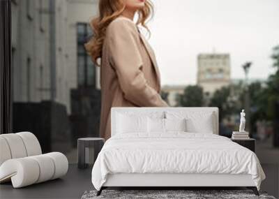 Portrait of young beautiful woman with long blonde hair in beige trench coat with a bag on the city street Wall mural