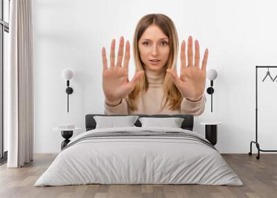 Serious blond girl keeps palms of both hands forward at camera, makes forbid sign, extends arms in stop sign Wall mural