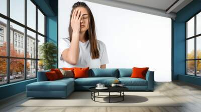 Young woman covers face, feels fatigue, needs good rest, has sleepy expression. Weariness and people. Copy space Wall mural