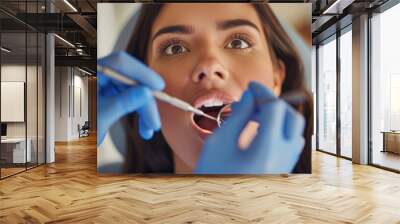 Face of calm young woman with white skin, dark brown hair and open mouth close-up of dentist doing dental examination with dental mirror and blue medical gloves Wall mural